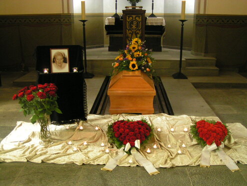 Aufgebahrter Sarg mit Blumenschmuck, Kerzen und einem Bild an einem Traueraltar in einer Kirche.