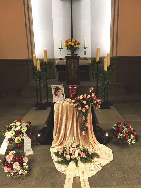 Gedenken an den Verstorbenen: Blumen, Kerzen und ein Foto auf einem Tisch in einem festlich dekorierten Raum.