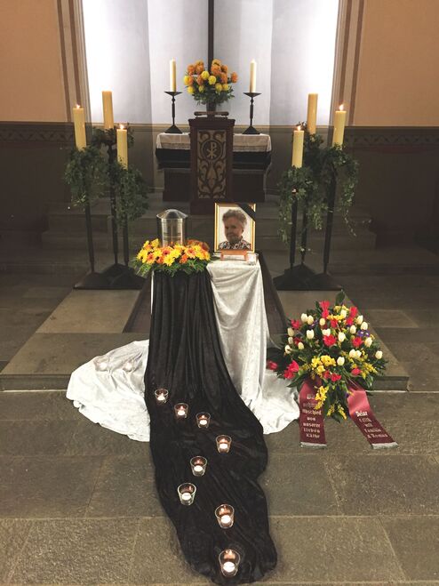 Kerze beleuchteter Altar mit Blumen, einem Portr&auml;t und einem Gedenkbereich in einer ged&auml;mpften Umgebung.