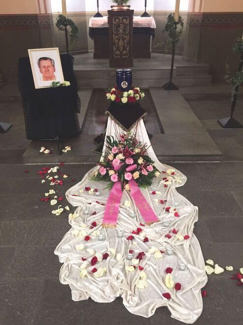 Blumenschmuck und ein Foto auf einem Altar, umgeben von Rosenbl&auml;ttern und einer wei&szlig;en Tuchdecke.
