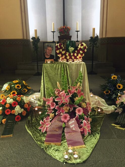 Gedenkaufenthalt mit Blumenarrangements, Kerzen und einem Foto auf einem Tisch in einer Kirche.