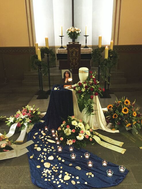Gedenkst&auml;tte mit Blumen, Kerzen und einem Portrait, umgeben von einer blauen Decke und Dekorationen.