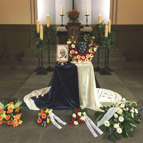 Andenkenaltar mit Blumen, Kerzen und Portr&auml;t einer Person in einem stilvollen, festlichen Raum.