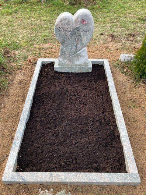 Grabbereich mit herzf&ouml;rmigem Steinsarg und frischer Erde auf einem ruhigen Friedhof.