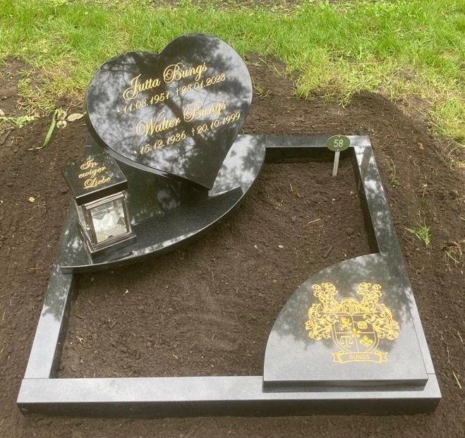 Granitgrabmal in Herzform mit den Namen Jutta und Walter Bungs sowie einer Laterne und einem Wappen auf schwarzem Untergrund.