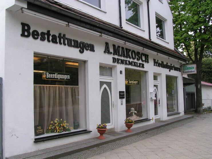 Fassade eines Bestattungsunternehmens mit Schildern und dekorativen Töpfen auf dem Gehweg.