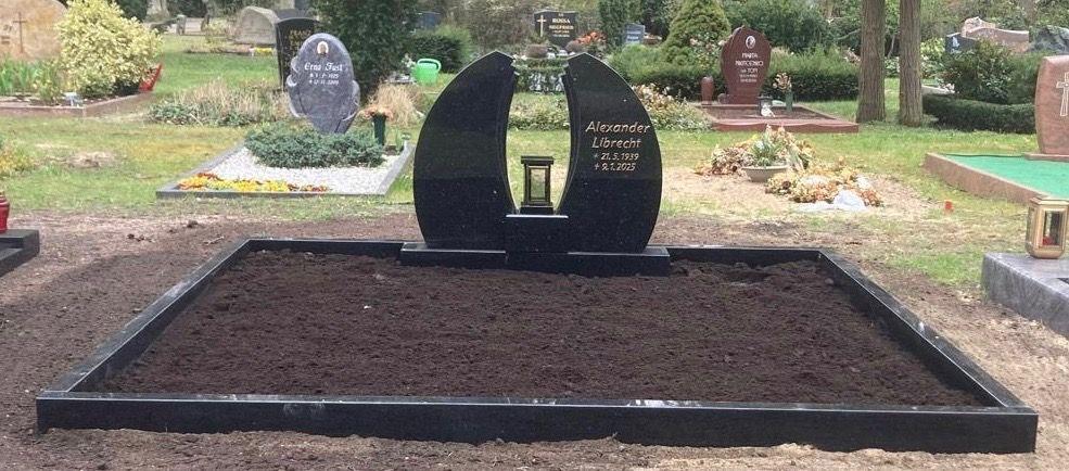 Schwarzes Grabmal mit darauf eingraviertem Namen und Daten, umgeben von frischem Erdboden auf einem Friedhof.