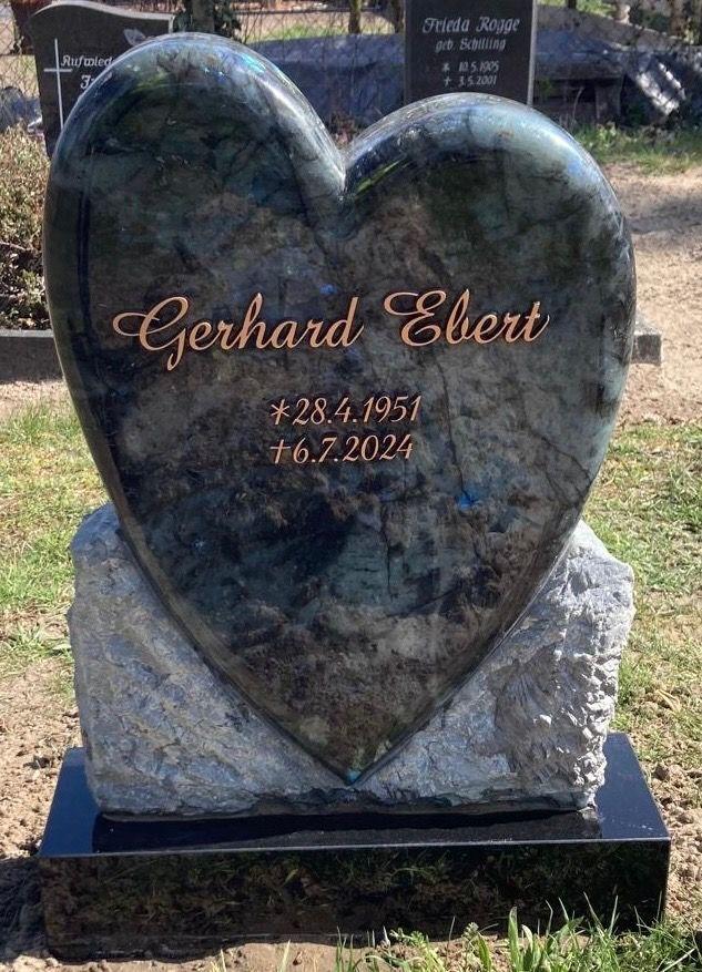 Granitgrabstein in Herzform mit Inschrift &bdquo;Gerhard Ebert, *28.4.1951, &dagger;6.7.2024&ldquo; auf steiniger Basis.