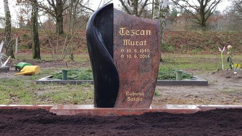 Grabstein aus schwarzem und rotem Granit mit Inschrift &bdquo;Tezcan Murat, 2.10.1940 - 10.6.2014&ldquo; in einem Friedhof.