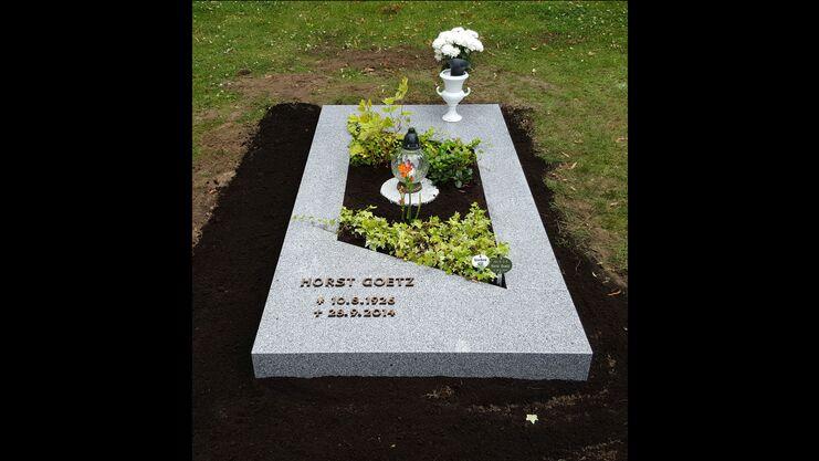 Granitgrabstein mit der Inschrift &bdquo;HORST G&Ouml;TZ&ldquo; und einem Blumenschmuck in einem gepflegten Grabbereich.