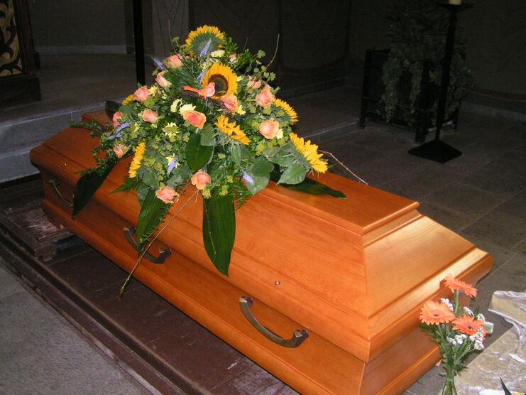 Holzene Urne mit einer bunten Blumenarrangement darauf, umgeben von einer ruhigen, schlichten Umgebung.