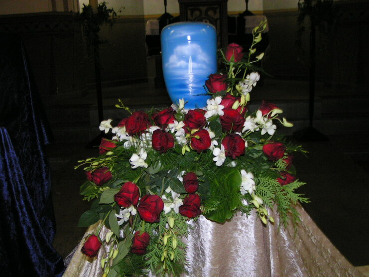 Bunte Blumenarrangements mit roten Rosen und wei&szlig;en Orchideen umgeben eine blaue Urne in einer Kirche.