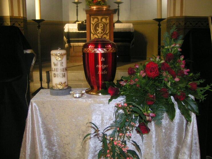Tisch mit Urne, Kerze und Blumenarrangement in einem w&uuml;rdevollen Raum.