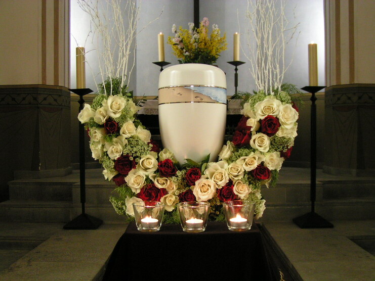 Wei&szlig;er Urne umgeben von roten und wei&szlig;en Rosen, Kerzen und Pflanzen in einem stilvoll dekorierten Raum.