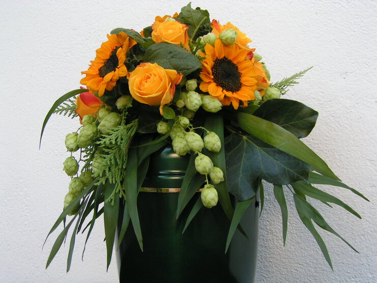 Bunter Blumenstrau&szlig; mit Sonnenblumen, Oranget&ouml;nen und gr&uuml;nem Laub in einem gr&uuml;nen Beh&auml;lter.