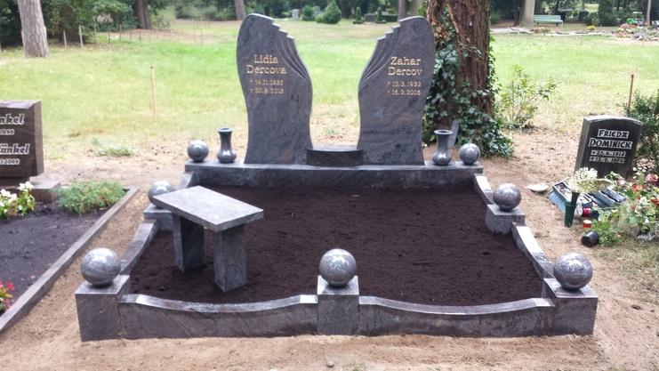 Grabstein mit zwei monumentalen Steinen, umgeben von Rasen und runden Steinstatuen. Zwischen den Steinen eine kleine Bank.