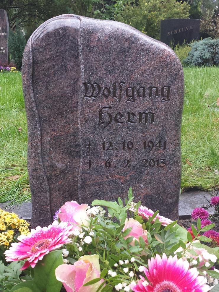 Grabstein mit dem Namen "Wolfgang Herm" und den Daten von Geburt und Tod, umgeben von bunten Blumen.