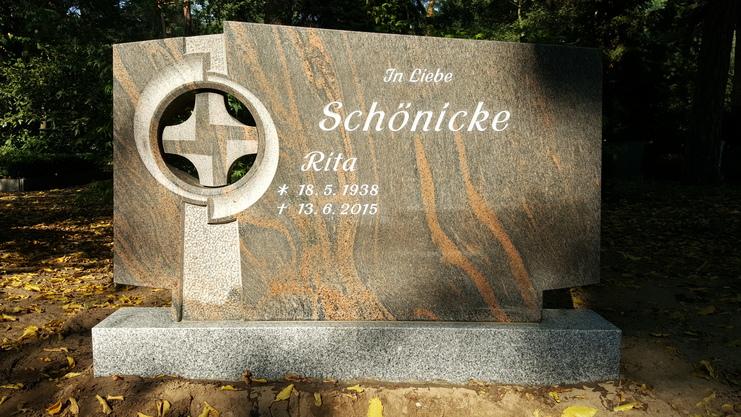 Granitgrabstein mit Kreuzen und Inschrift: &bdquo;In Liebe, Sch&ouml;nicke, Rita, * 18. 5. 1938, &dagger; 13. 6. 2015&ldquo; auf gr&uuml;nem Hintergrund.