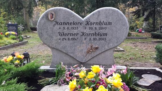 Granitgrabstein in Herzform mit Namen und Lebensdaten von Hannelore und Werner Kornblum, umgeben von bunten Blumen.