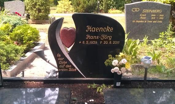 Schwarzer Grabstein mit Herzform, Inschrift &bdquo;Haencke Hans-J&ouml;rg&ldquo; und Blumenarrangement auf einer Grabst&auml;tte.