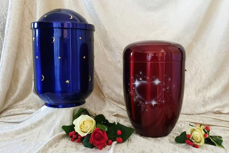Zwei Urnen in Blau und Rot stehen auf einem weißen Stoff, umgeben von roten und weißen Rosen.