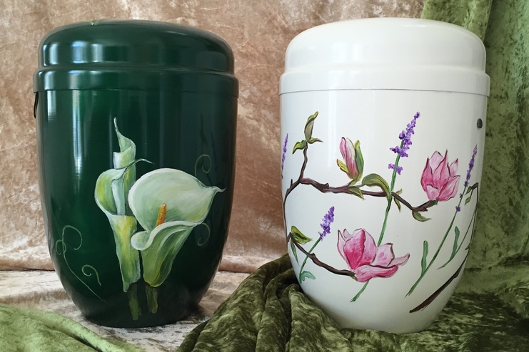 Zwei handbemalte Becher: ein gr&uuml;ner mit einer Calla-Lilie und ein wei&szlig;er mit Magnolien- und Lavendelmotiven.