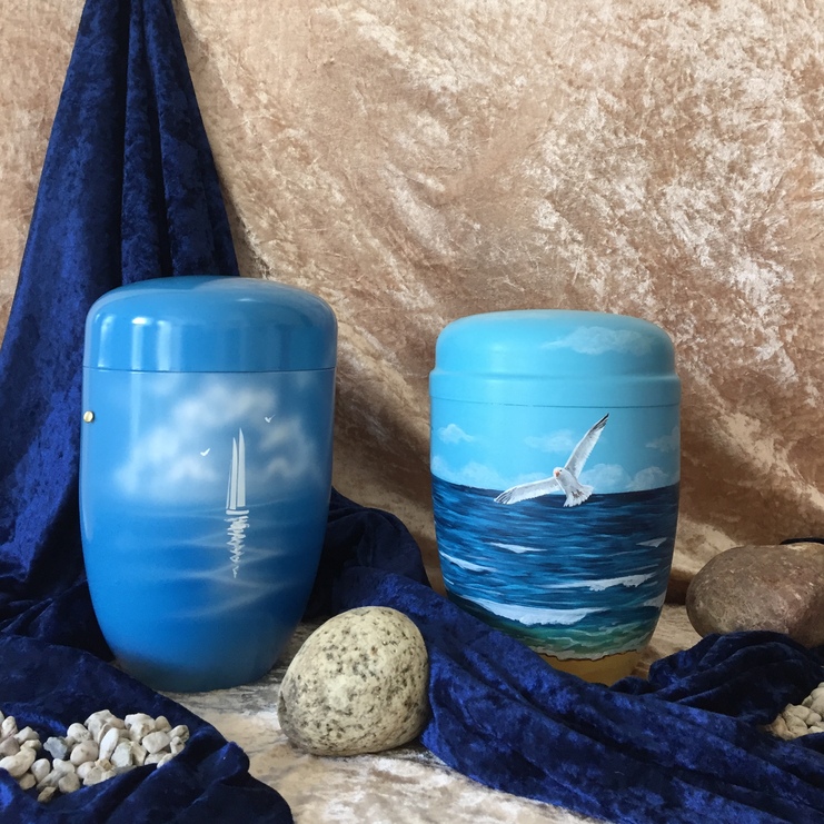 Zwei blaue Urnen mit maritimen Motiven stehen vor einem goldenen Hintergrund und umgeben von Steinen und blauer Stoffdeko.